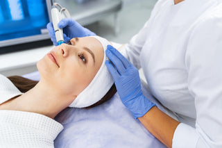 A person receiving a HydraFacial treatment, which includes steps like double cleanse & steam, dermaplane, sonic scrubber, deep cleanse, skin mask, mesotherapy, radio frequency collagen stimulation, LED mask, and lymph drainage massage.