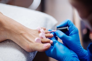 Person getting pedicure with blue gloves applying nail polish to toes.
