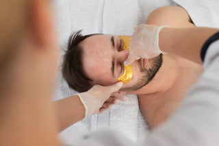 A man receiving a facial treatment, with a focus on his face which is being cleaned with a product by a professional.