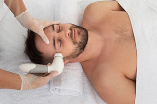 Man receiving a facial treatment with a device on a white towel.