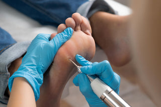Person receiving a pedicure with blue gloves using a nail drill.