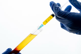 Hand in blue glove holding a syringe with yellow liquid against a white background