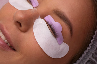 Close-up of a person undergoing a lash lift treatment, with false eyelashes applied and eye patches on